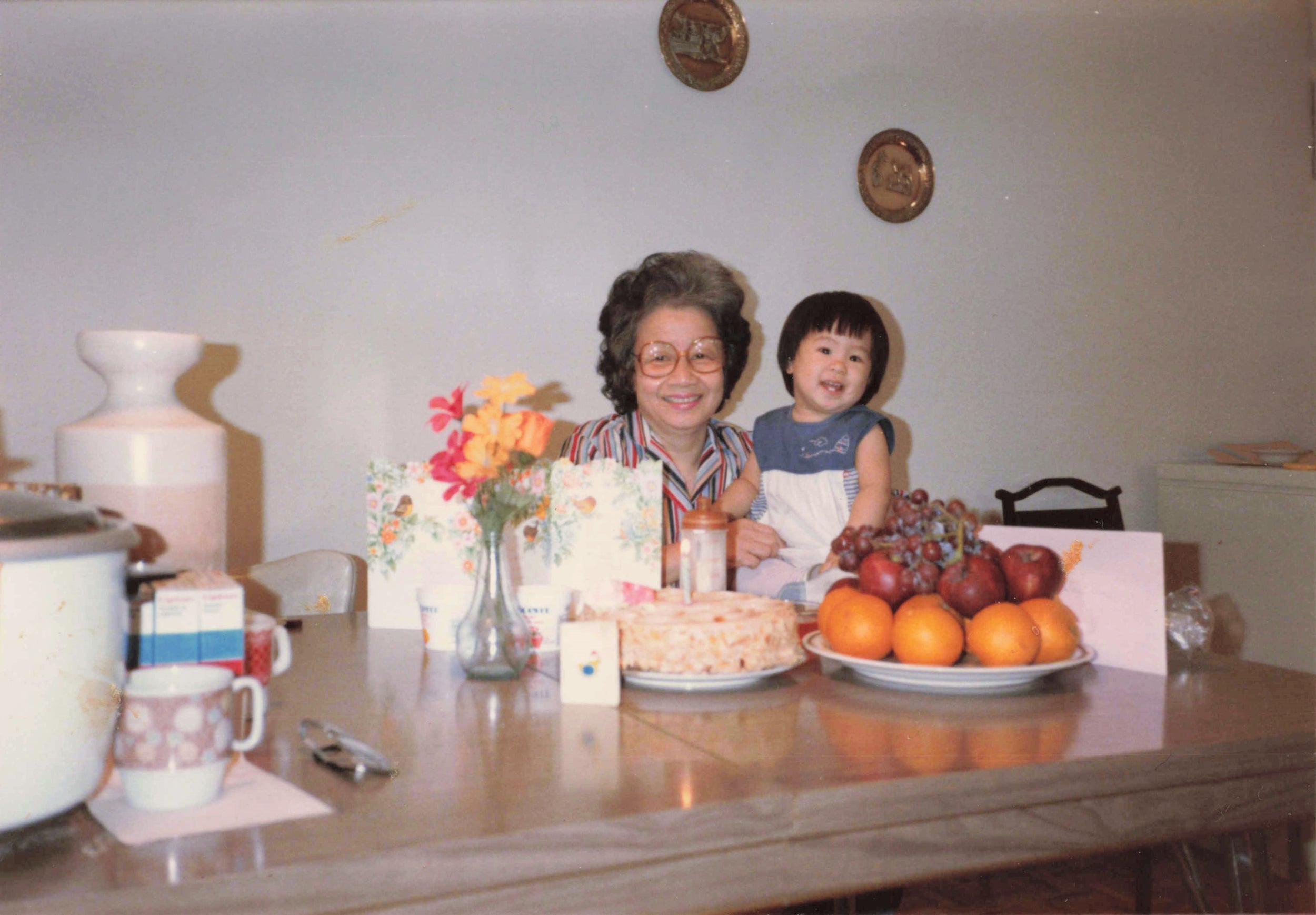 A childhood photo of Kat Lieu, the founder of the Subtle Asian Baking community and cookbook author of Modern Asian Baking At Home, with their grandmother at a dining table.